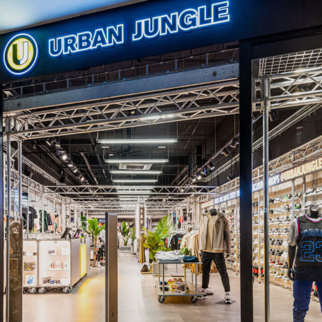 Urban Jungle store entrance with illuminated blue sign, exposed steel truss ceiling and industrial shop floor