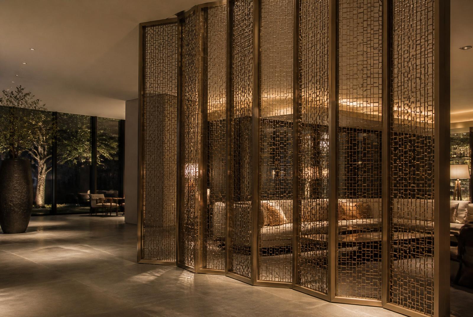 Full-height bronze mesh screens dividing a warmly lit hotel interior