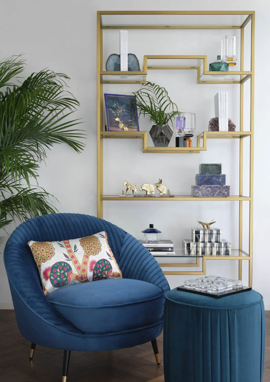 Blue lounge chair beside a brass display shelf and plants