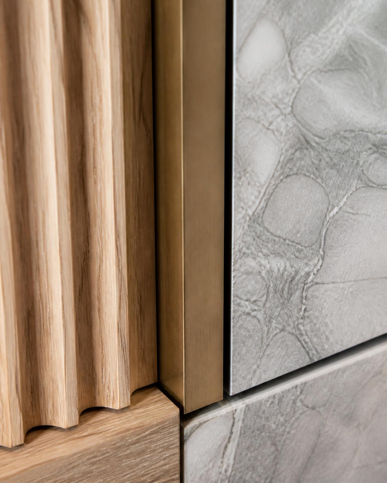 Close detail of fluted oak, bronze and honed stone meeting in a single joint