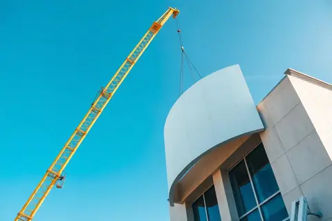 Curved facade panel being lifted into position by crane