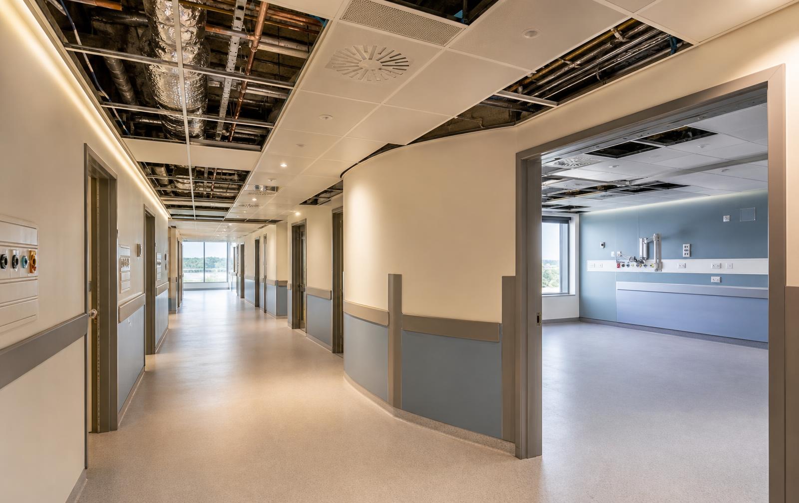 Hospital ward corridor with accessible ceiling panels open showing ductwork and medical gas pipework