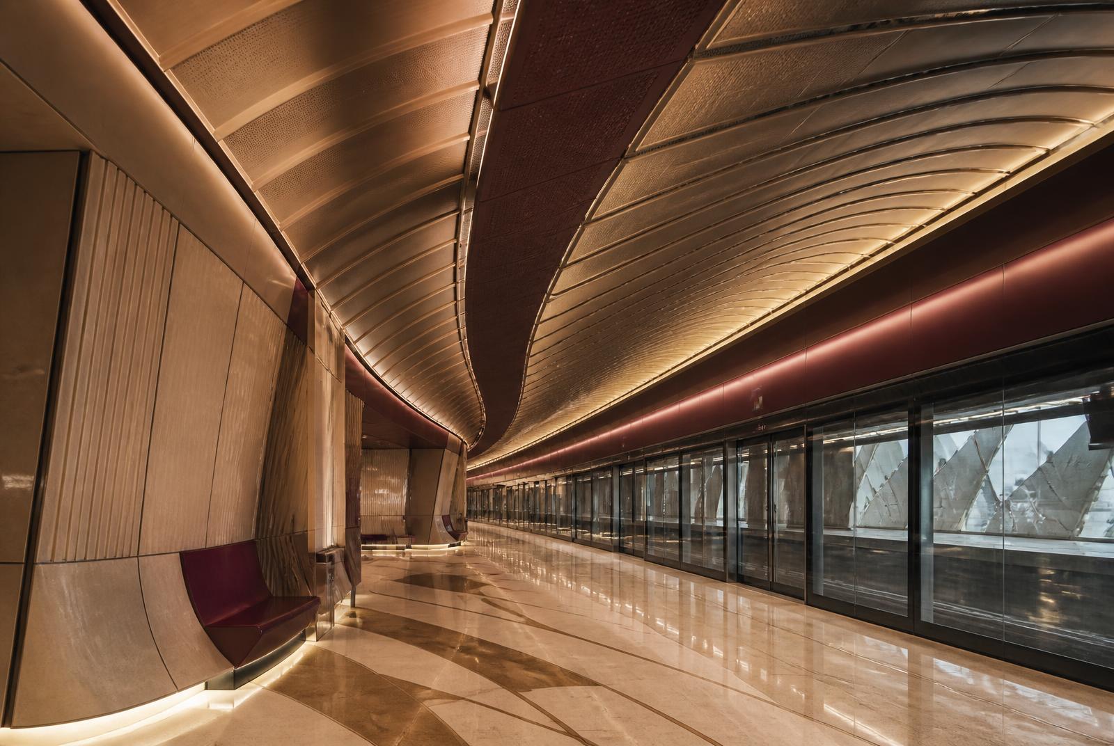Metro station platform with curved bronze ceiling, stone floor and platform screen doors